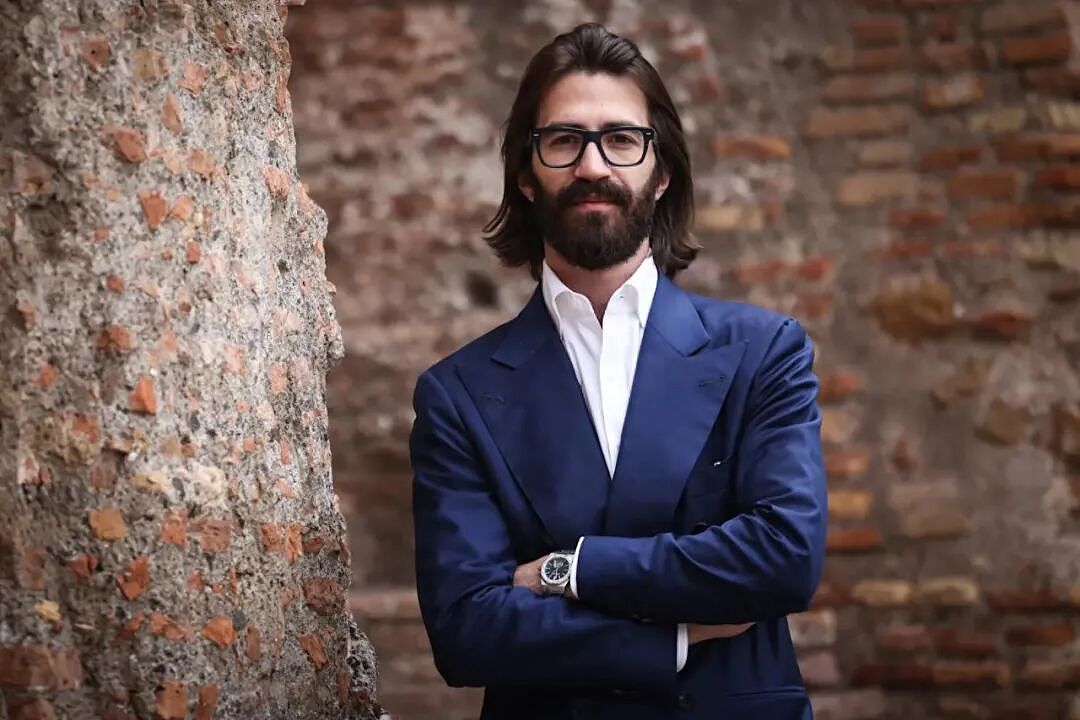Leonardo Maria Del Vecchio 身著深色西裝站在磚牆旁