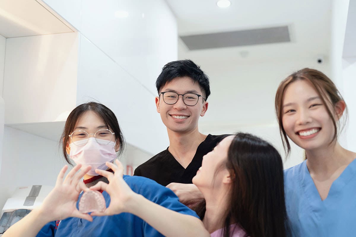 WOW Dental 官网图库中四位工作人员在诊疗室内展示牙齿模型